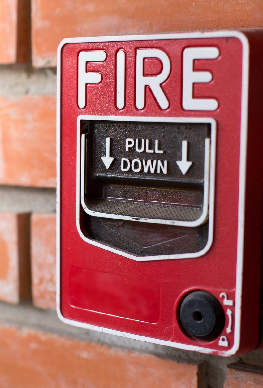 Manual emergency red fire alarm system box with push button placed on white shabby wall in light room of building